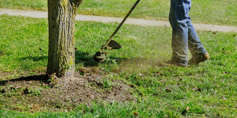 Trabajador realizando mantenimiento de áreas verdes con una desbrozadora en un condominio, asegurando la conservación del césped y la estética del entorno.