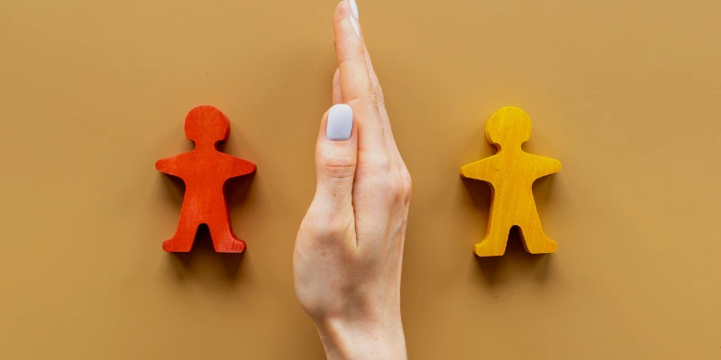 Mano separando dos figuras de madera de diferentes colores, representando la mediación y resolución de conflictos en la administración de condominios. Administración de Condominios: Gestión de Conflictos y Normativas | Mabinsa