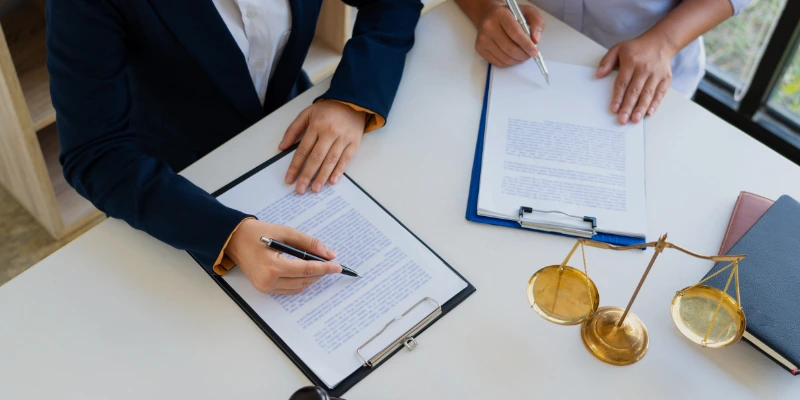 Dos personas firmando documentos legales relacionados con la administración profesional de condominios en una oficina con balanza de justicia.