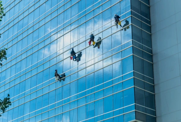 Especialista en limpieza realizando mantenimiento de vidrios en edificio corporativo con equipo de seguridad