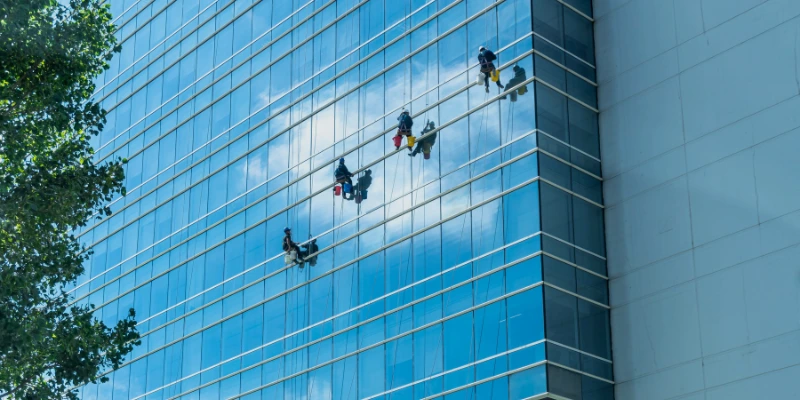 Especialista en limpieza realizando mantenimiento de vidrios en edificio corporativo con equipo de seguridad